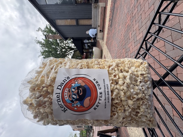 A big labeled bag of kettle corn on a rack in a brick plaza