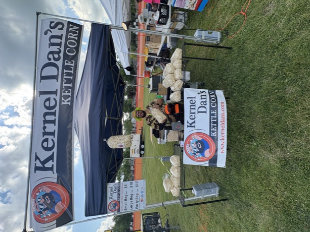 The Kernel Dan's tent, banner, and racks of bags at a festival